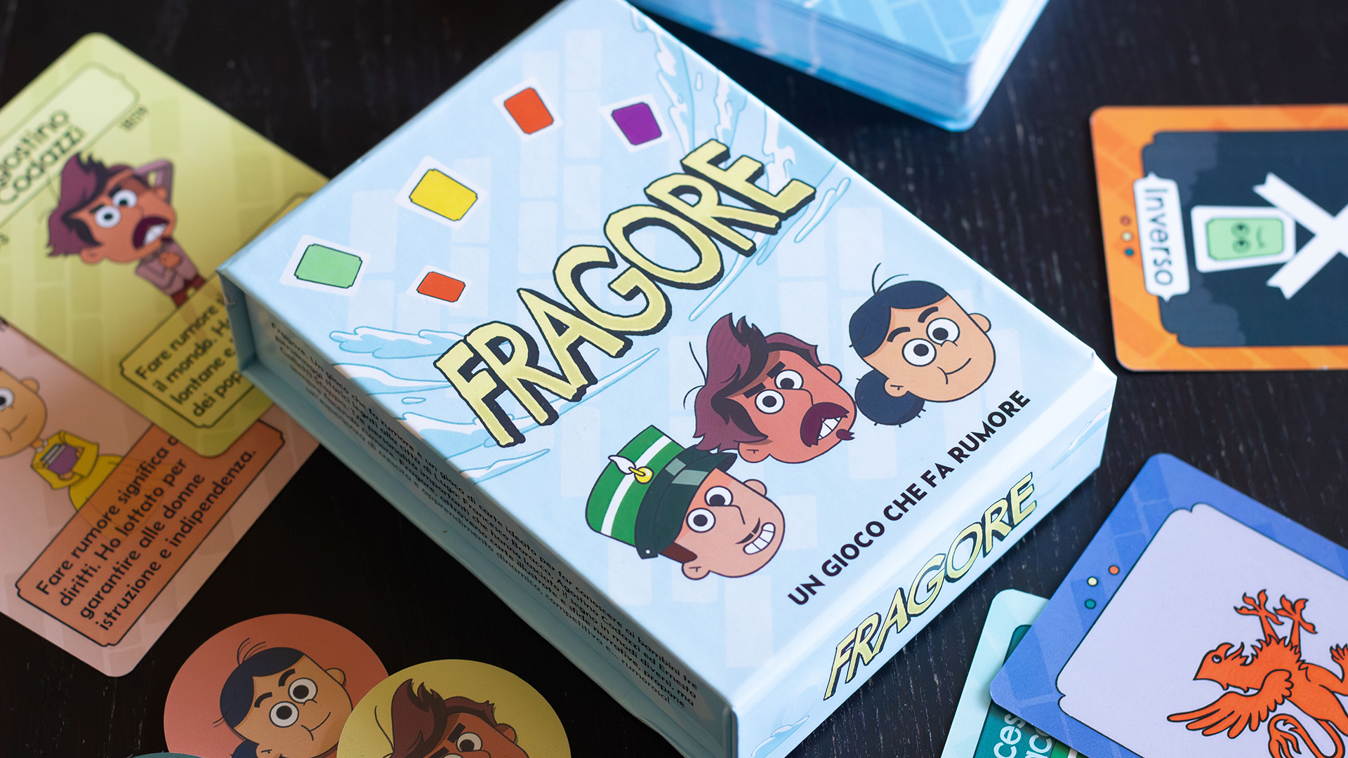 La scatola del gioco di carte Fragore circondata dalle carte dedicate ai tre personaggi